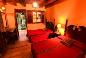 Ein Zimmer mit zwei roten Betten, einem Holztisch, einer Lampe und einer Gitarre.