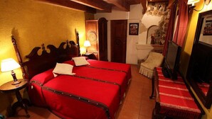Une chambre avec un lit en bois, deux tables de chevet avec des lampes, un mur en pierre, une chaise et un téléviseur.