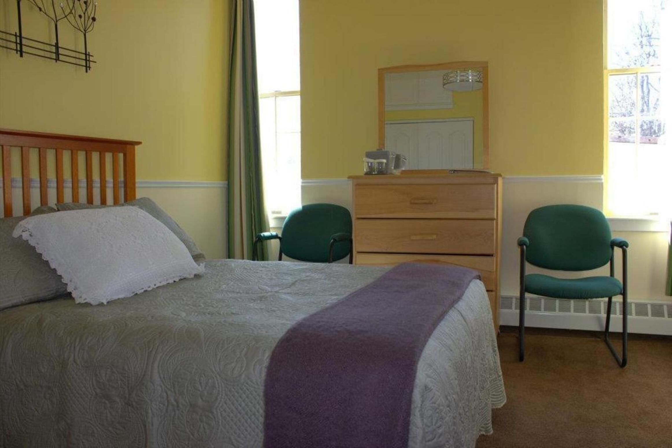 A bedroom with a bed, two chairs, a dresser, and a mirror.