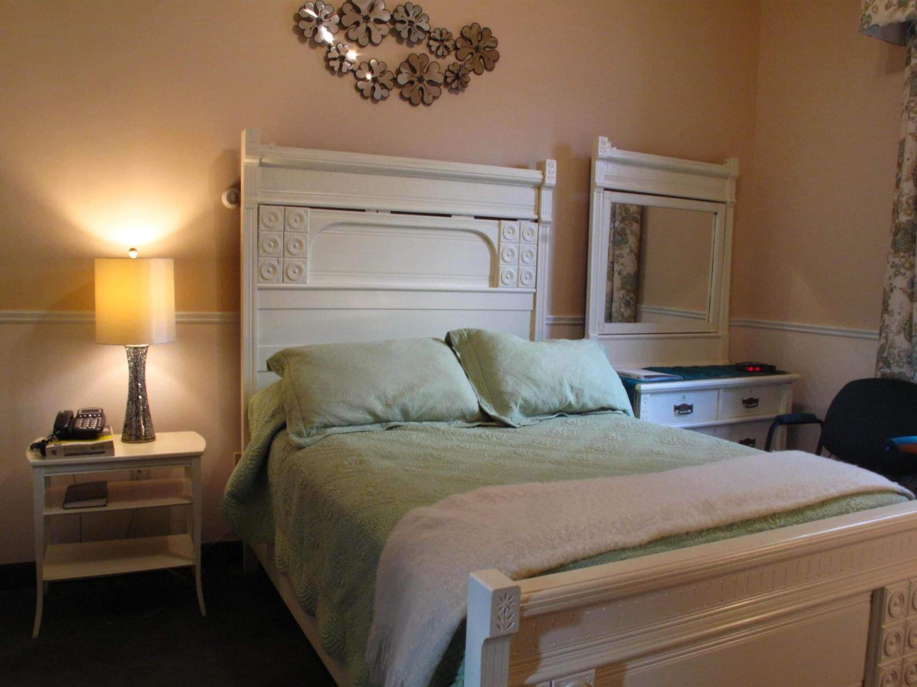 A hotel room with a bed, a bedside table with a lamp, a dresser, and a mirror.