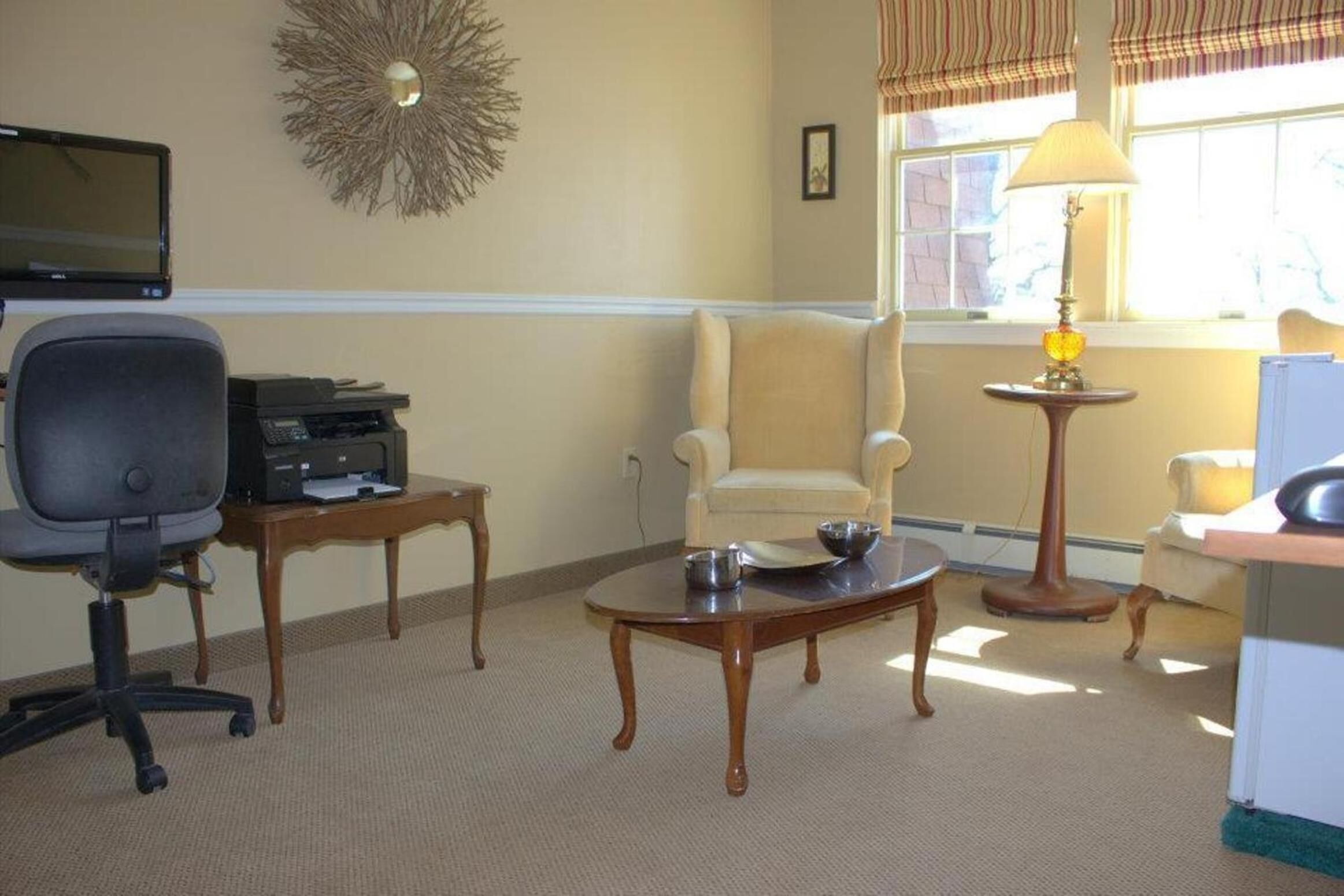 A room with a desk, office chair, and a round table with a lamp.