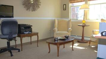 A room with a desk, office chair, and a round table with a lamp.