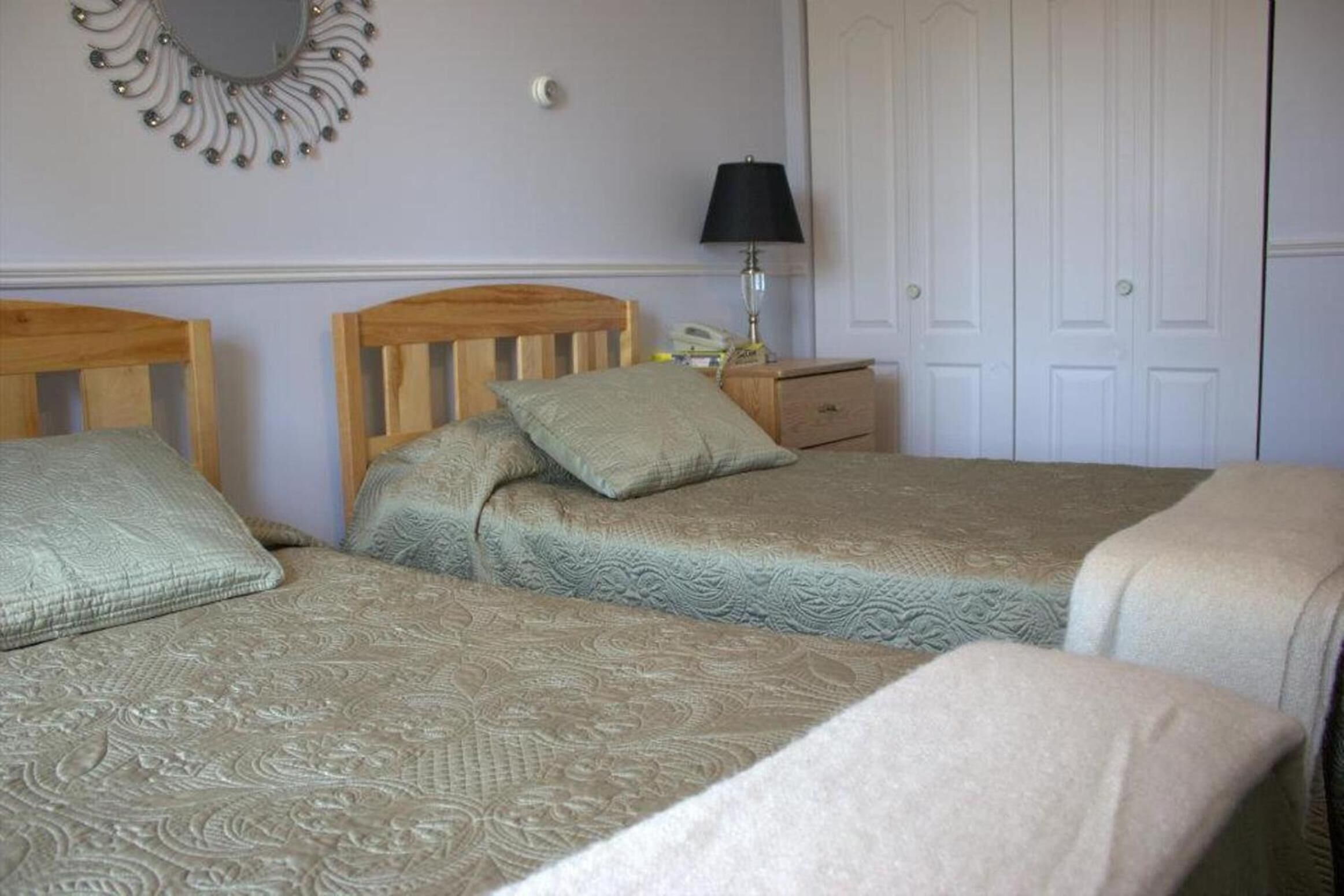 A bedroom with two single beds, a bedside table with a lamp, a mirror, and a wardrobe.