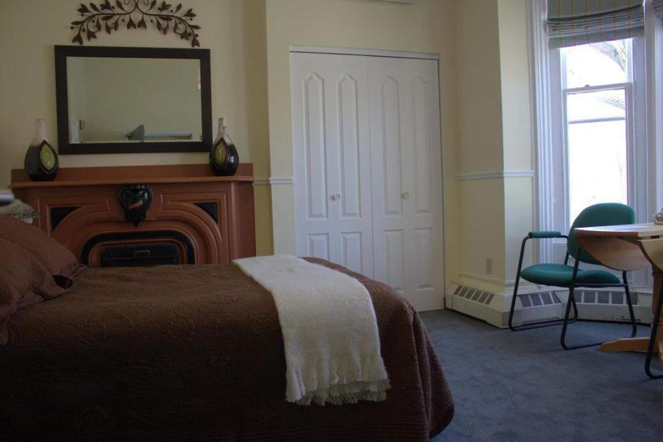 A bedroom with a bed, a dresser, a mirror, a white door, and a window with a view.