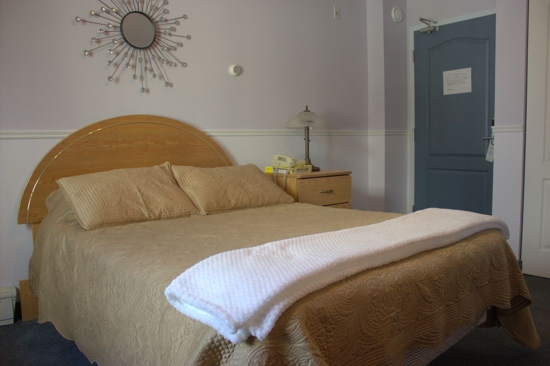 A neatly made bed with a wooden headboard, a bedside lamp, and a door in the background.