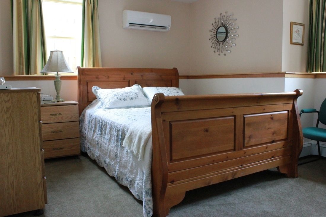 A bedroom with a wooden bed, a nightstand, a lamp, a dresser, and a chair.