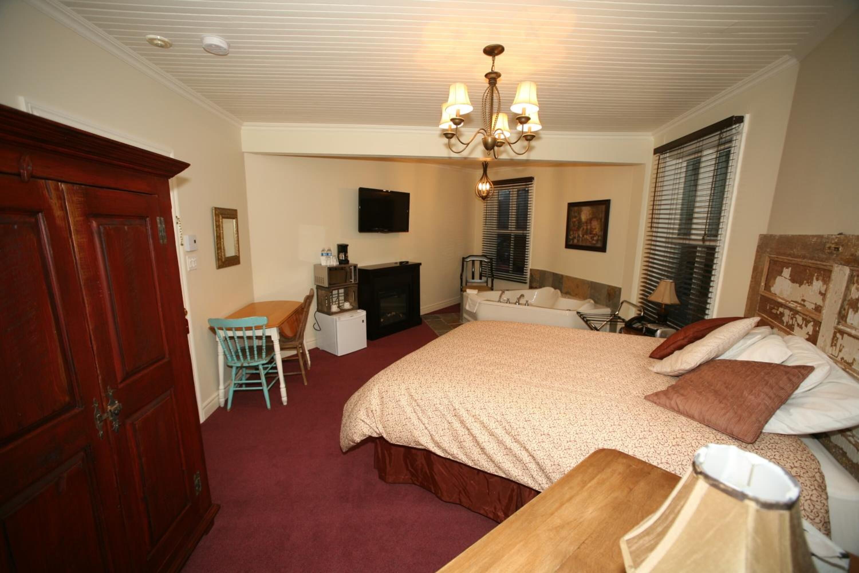 A bedroom with a large bed, a wooden desk, a chair, a television, and a fireplace.