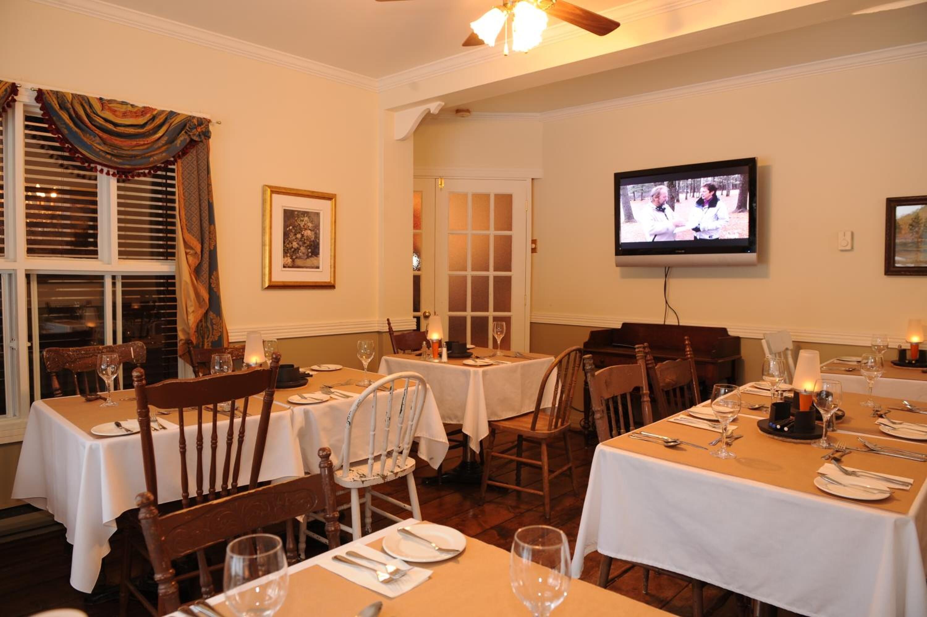 A dining area with tables set for two, chairs, and a television mounted on the wall.