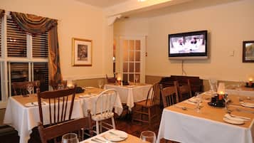 A dining area with tables set for two, chairs, and a television mounted on the wall.