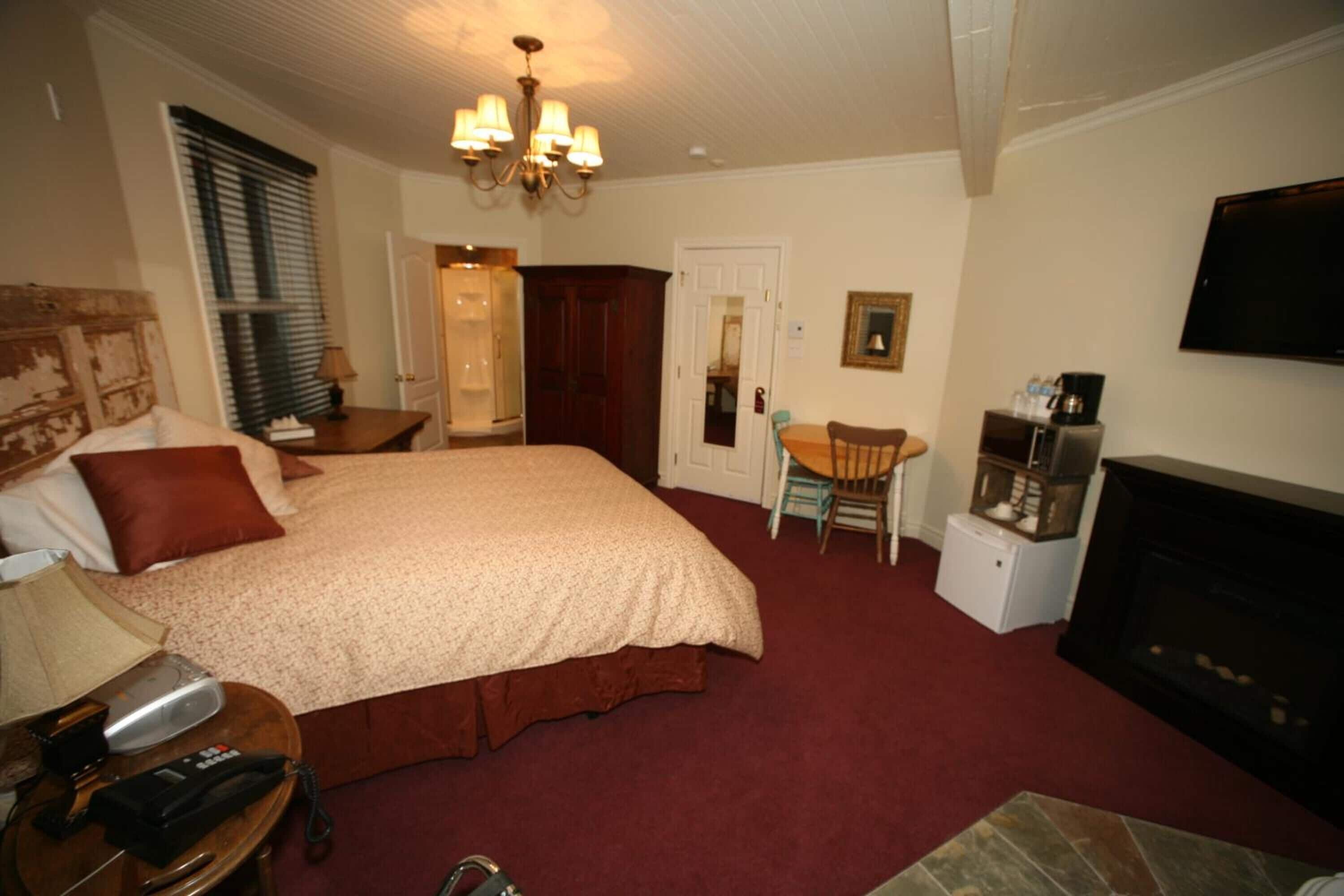 A hotel room with a large bed, a desk with a chair, a fireplace, and a television on the wall.