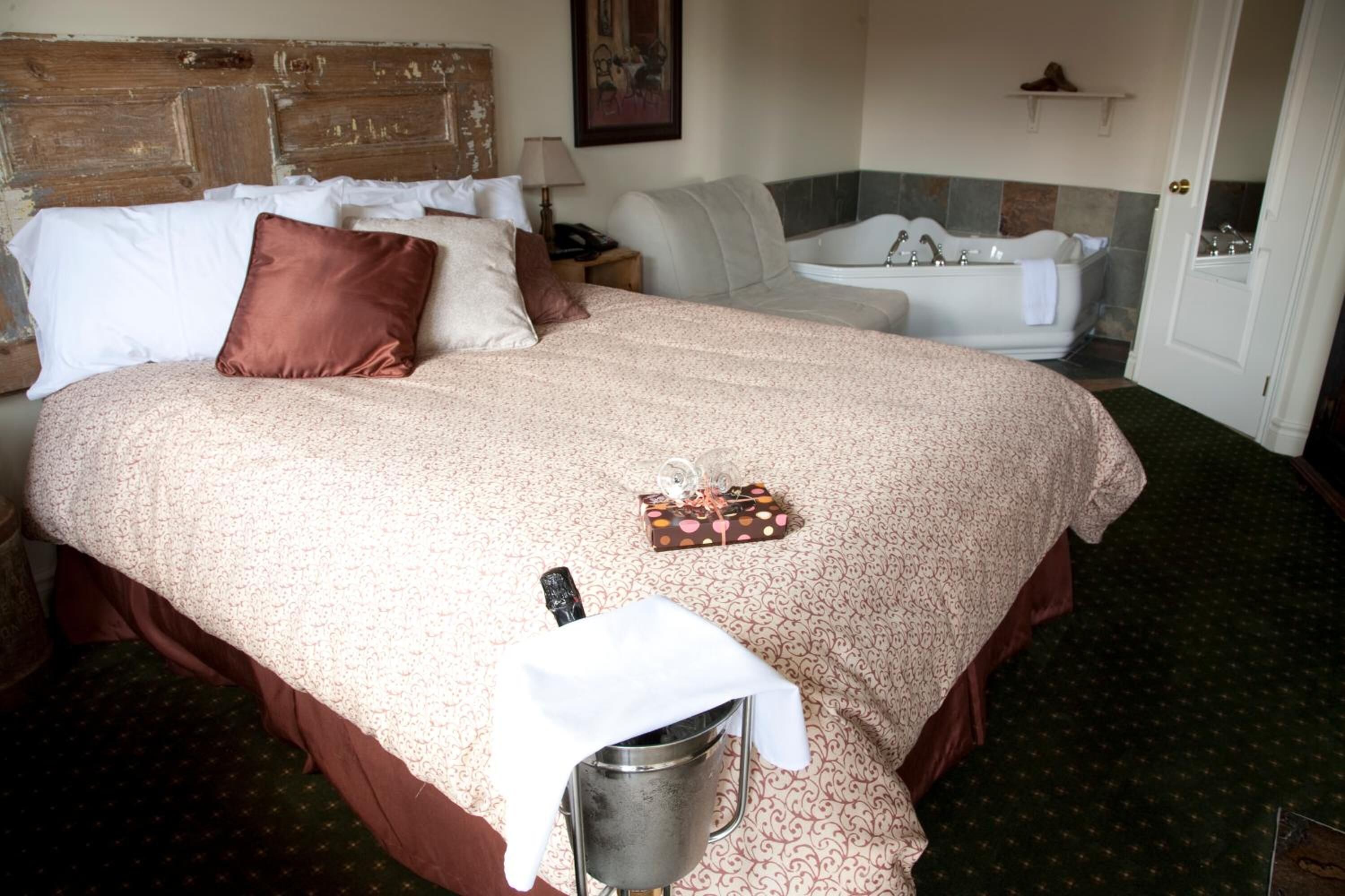 Una habitación de hotel con una cama grande, un baño con bañera y una pequeña mesa con un cubo.