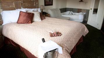 Una habitación de hotel con una cama grande, un baño con bañera y una pequeña mesa con un cubo.