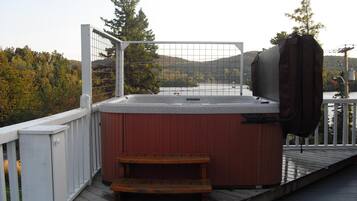 A hot tub on a wooden deck with a view of a lake and hills.