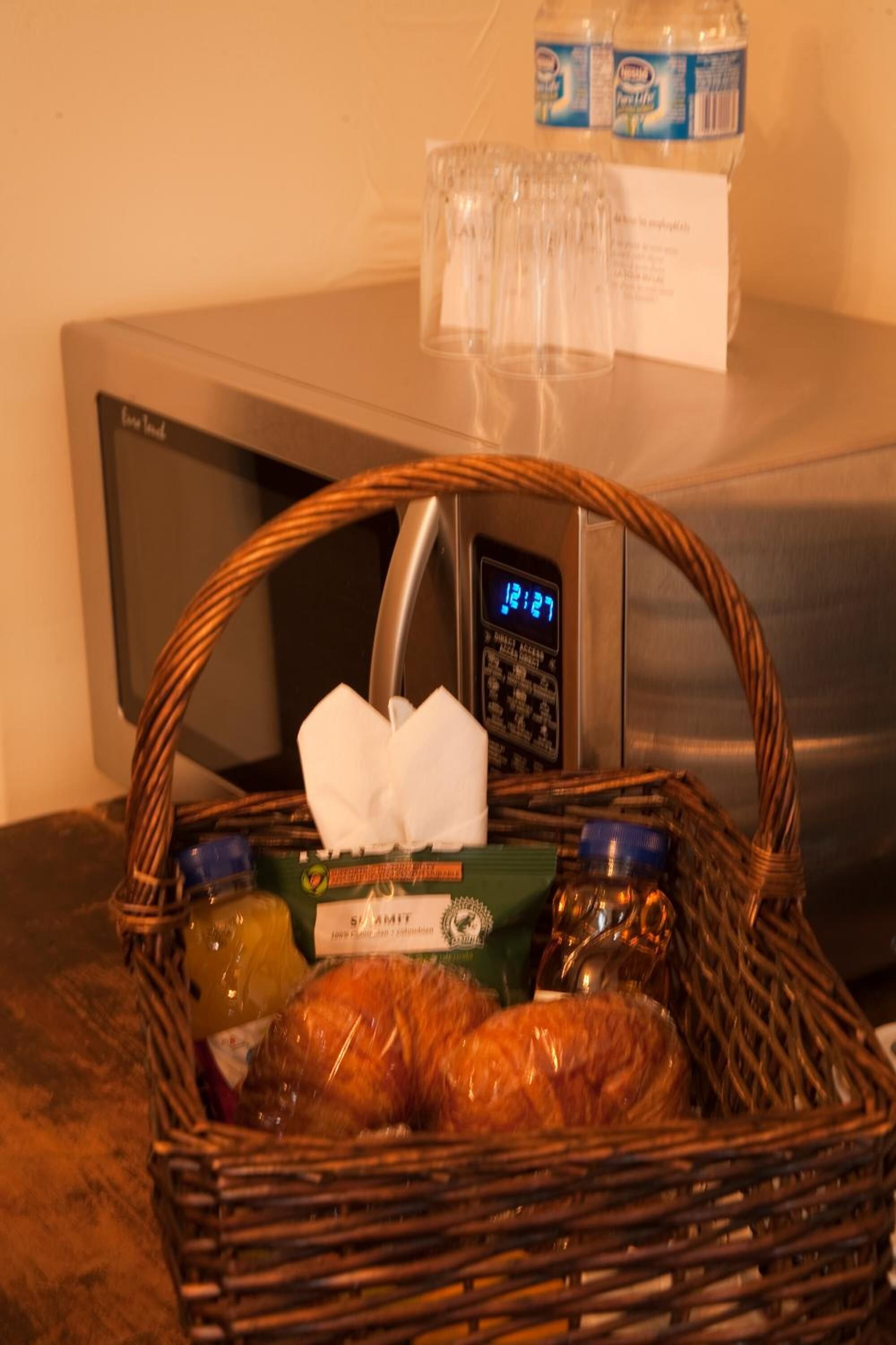 A basket with bread, a bottle, and a tissue on a counter next to a microwave and refrigerator.