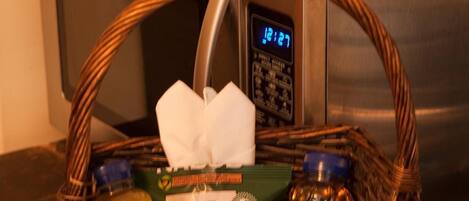 A basket with bread, a bottle, and a tissue on a counter next to a microwave and refrigerator.