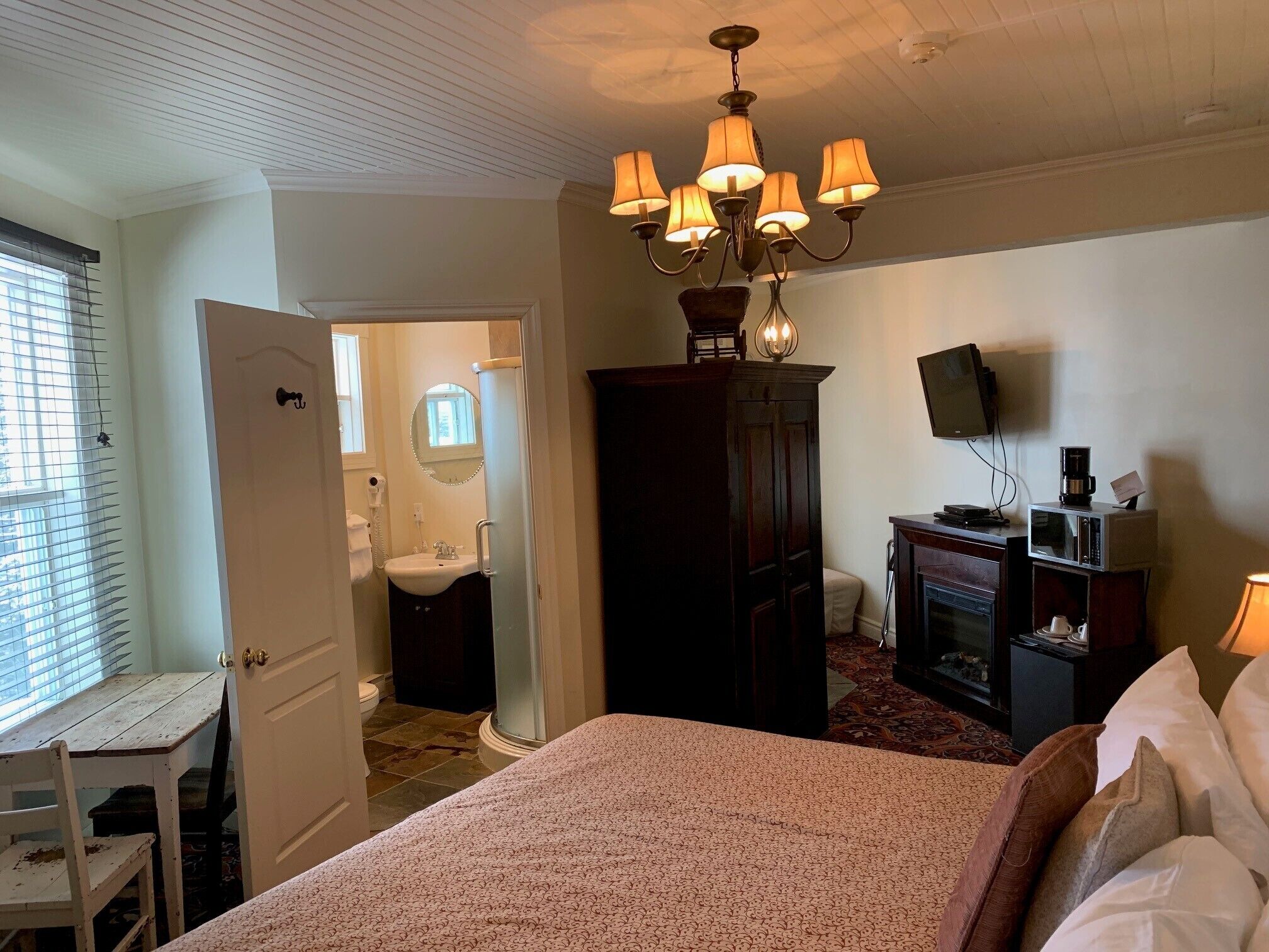 Un dormitorio con cama, escritorio, armario, televisión y candelabro.