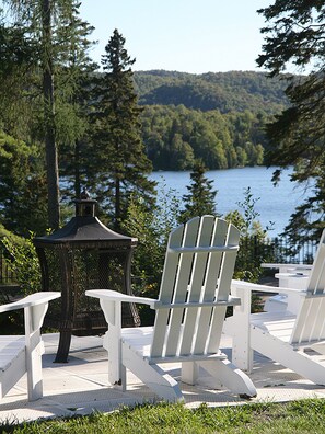 Un belvédère et des fauteuils Adirondack offrent une vue sur un lac, avec des collines boisées en arrière-plan.