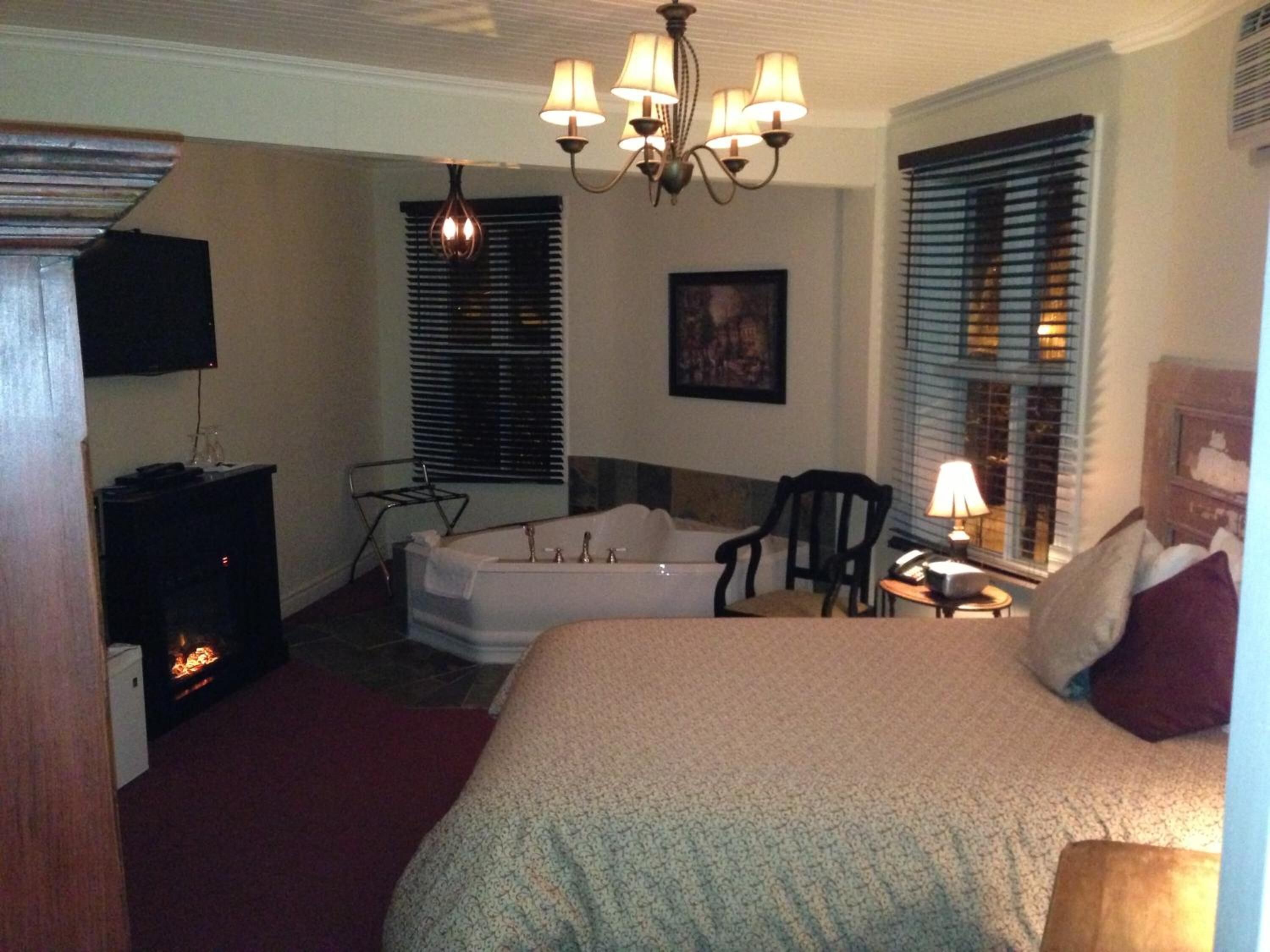 A hotel room with a large bed, a fireplace, a desk with a lamp, and a chair.