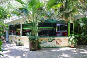 A small, green-roofed building with a mural of a tropical scene.