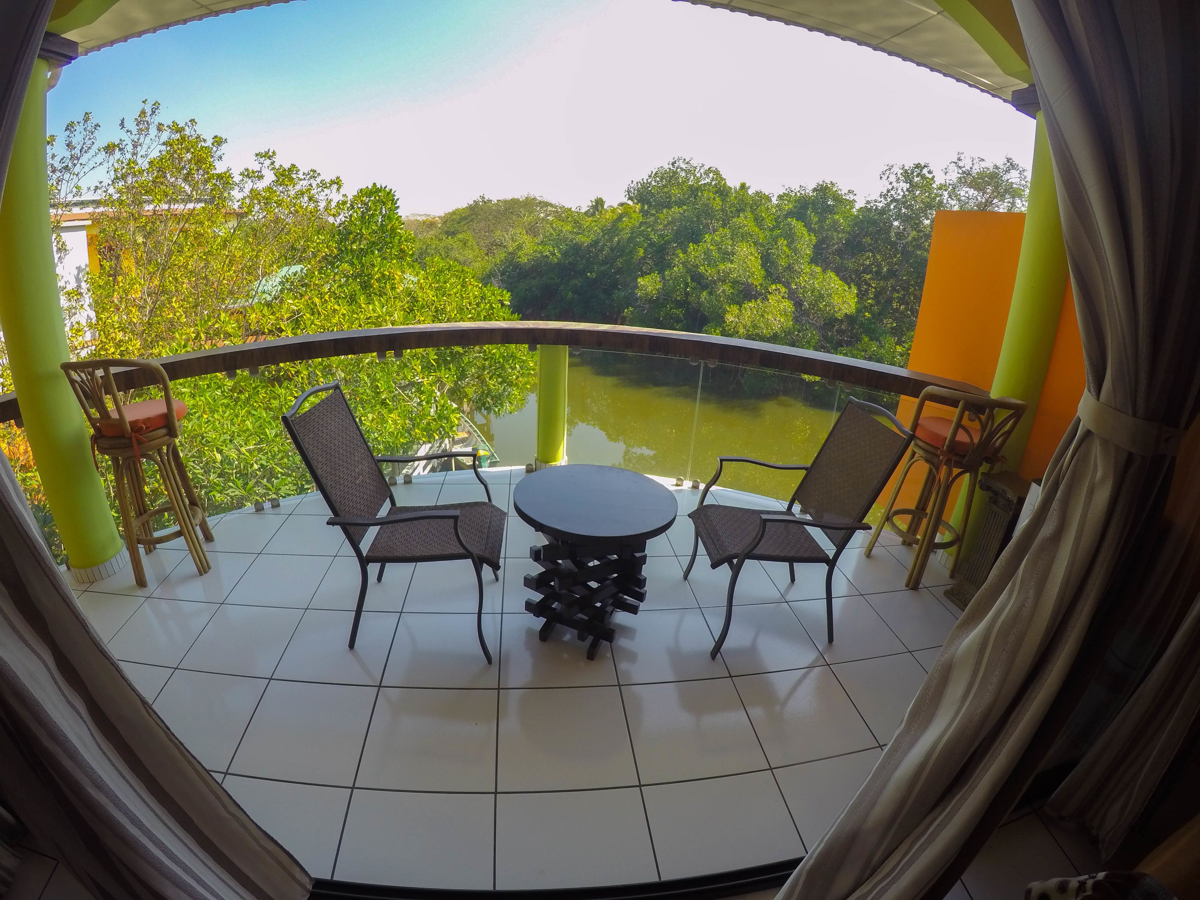Un balcon avec une table et des chaises, donnant sur une étendue d’eau et sur de la verdure.
