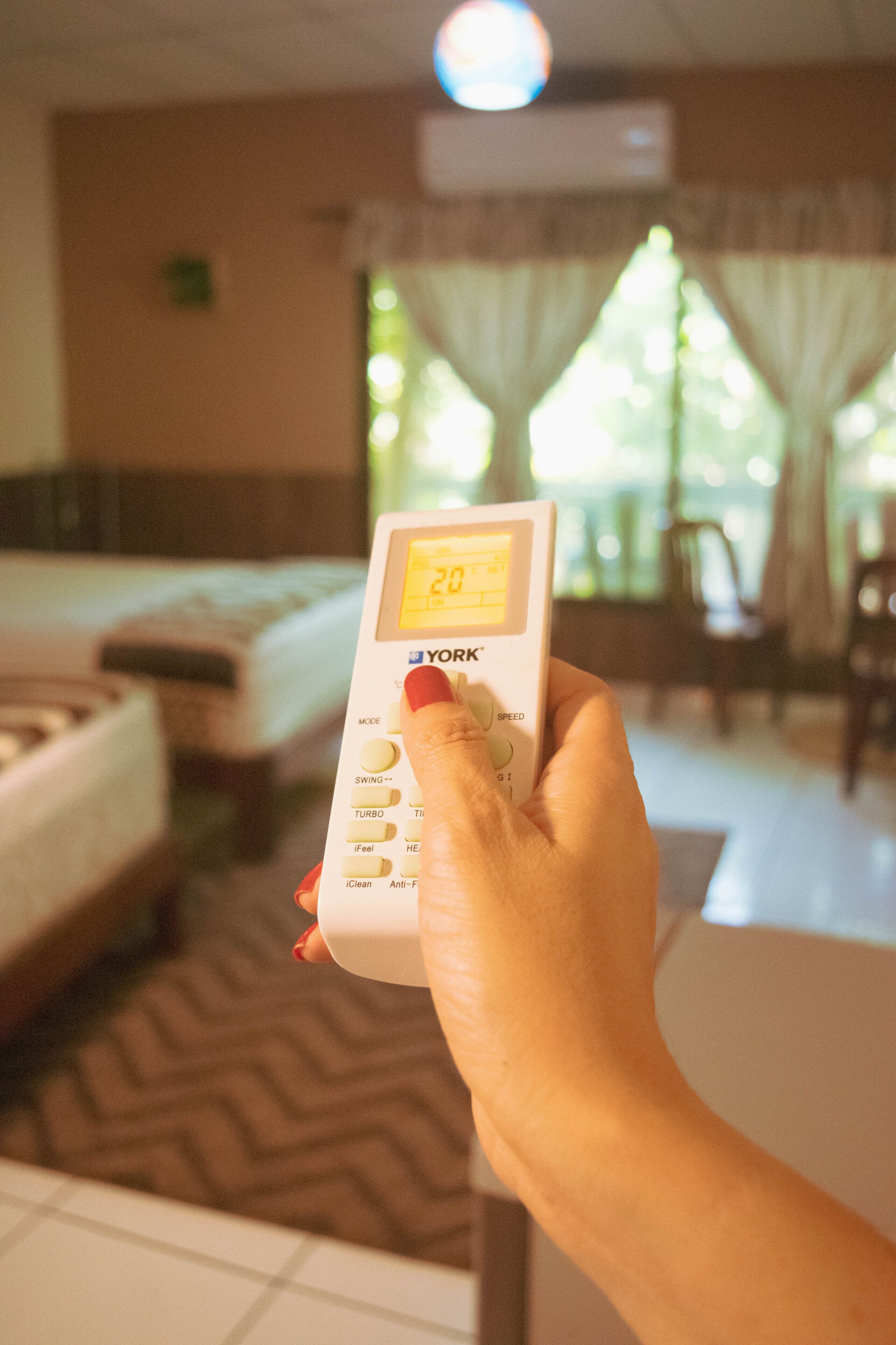 A hand holding a digital thermostat with a display showing 20 degrees.