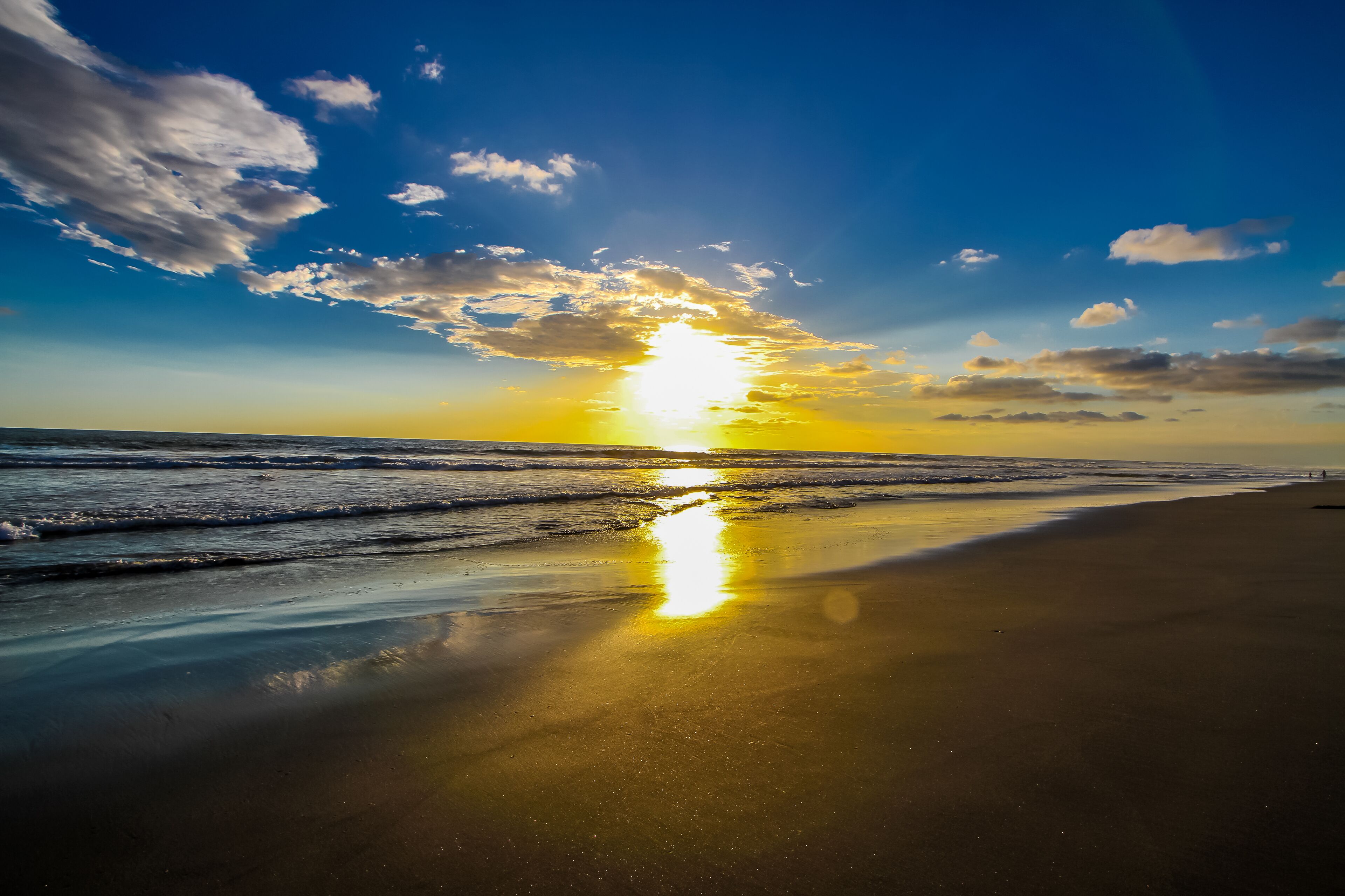 Una playa con un atardecer, olas y cielo despejado.