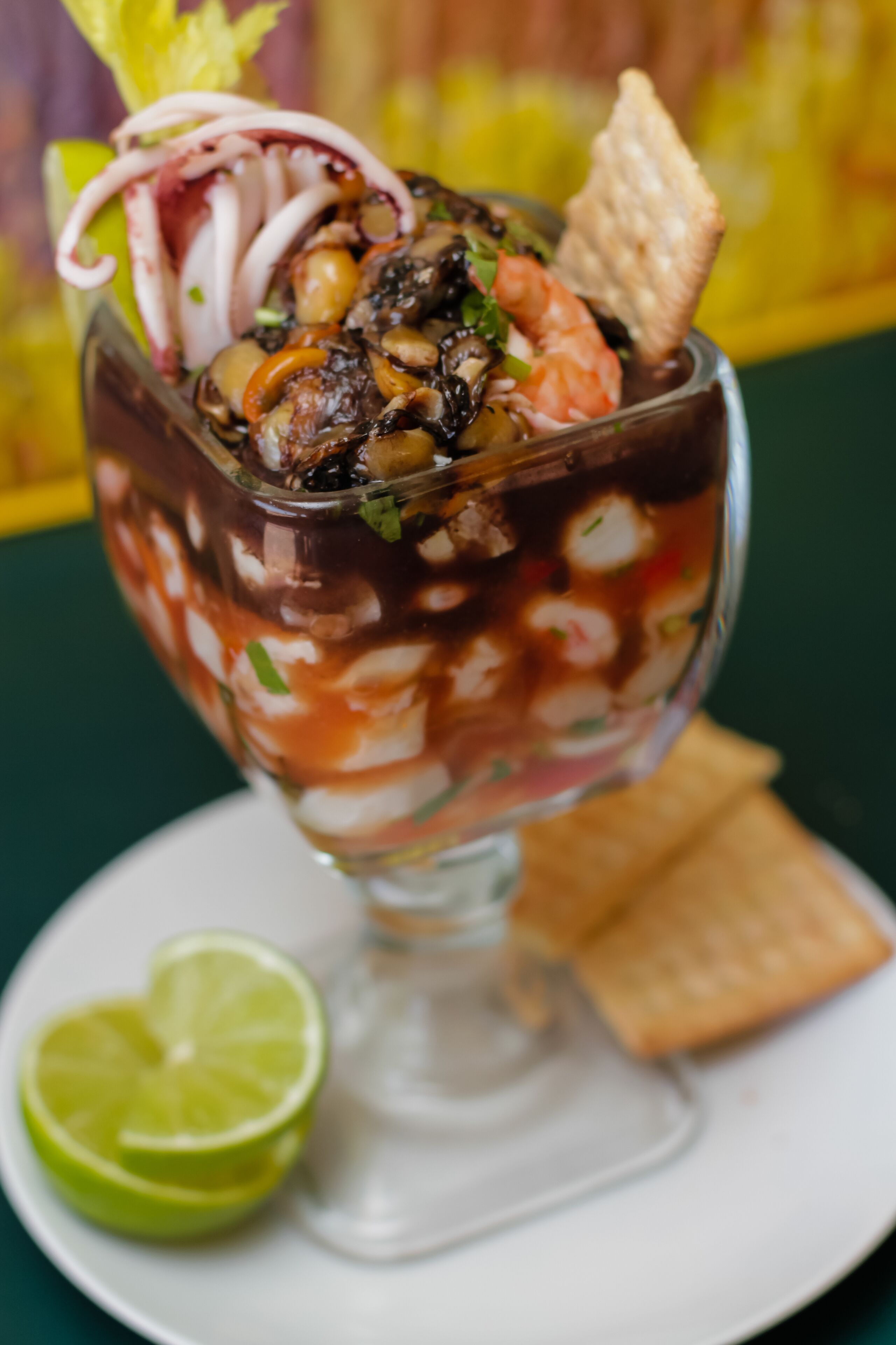 A dessert in a glass cup with a lime wedge and a cracker on the side.