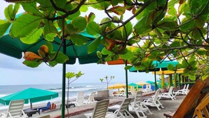 Un espace aménagé avec des chaises longues blanches et des parasols verts, situé au bord de la plage et offrant une vue sur l’océan.