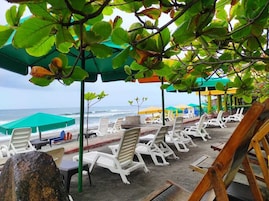 A beachside seating area with white lounge chairs and green umbrellas, overlooking the ocean.