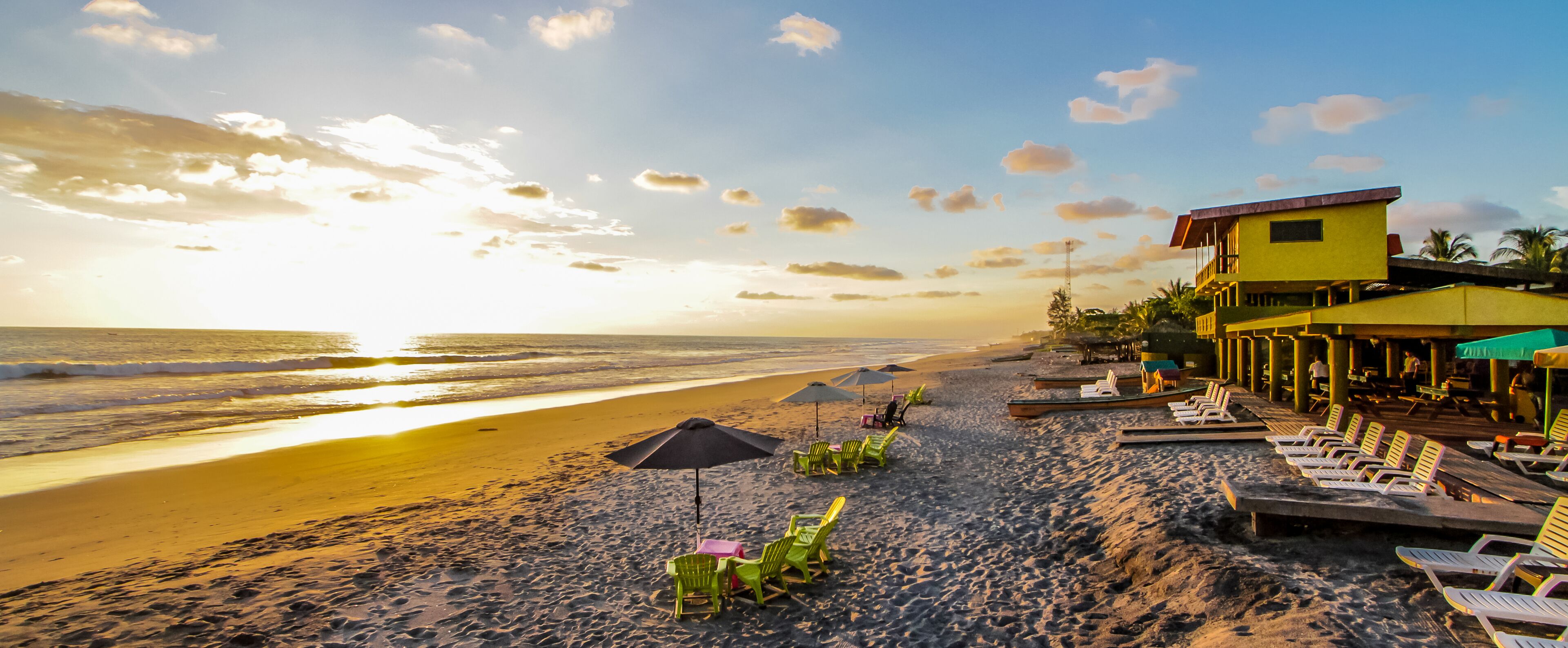 A beach with sun loungers, umbrellas, and a building with a balcony overlooking the ocean.
