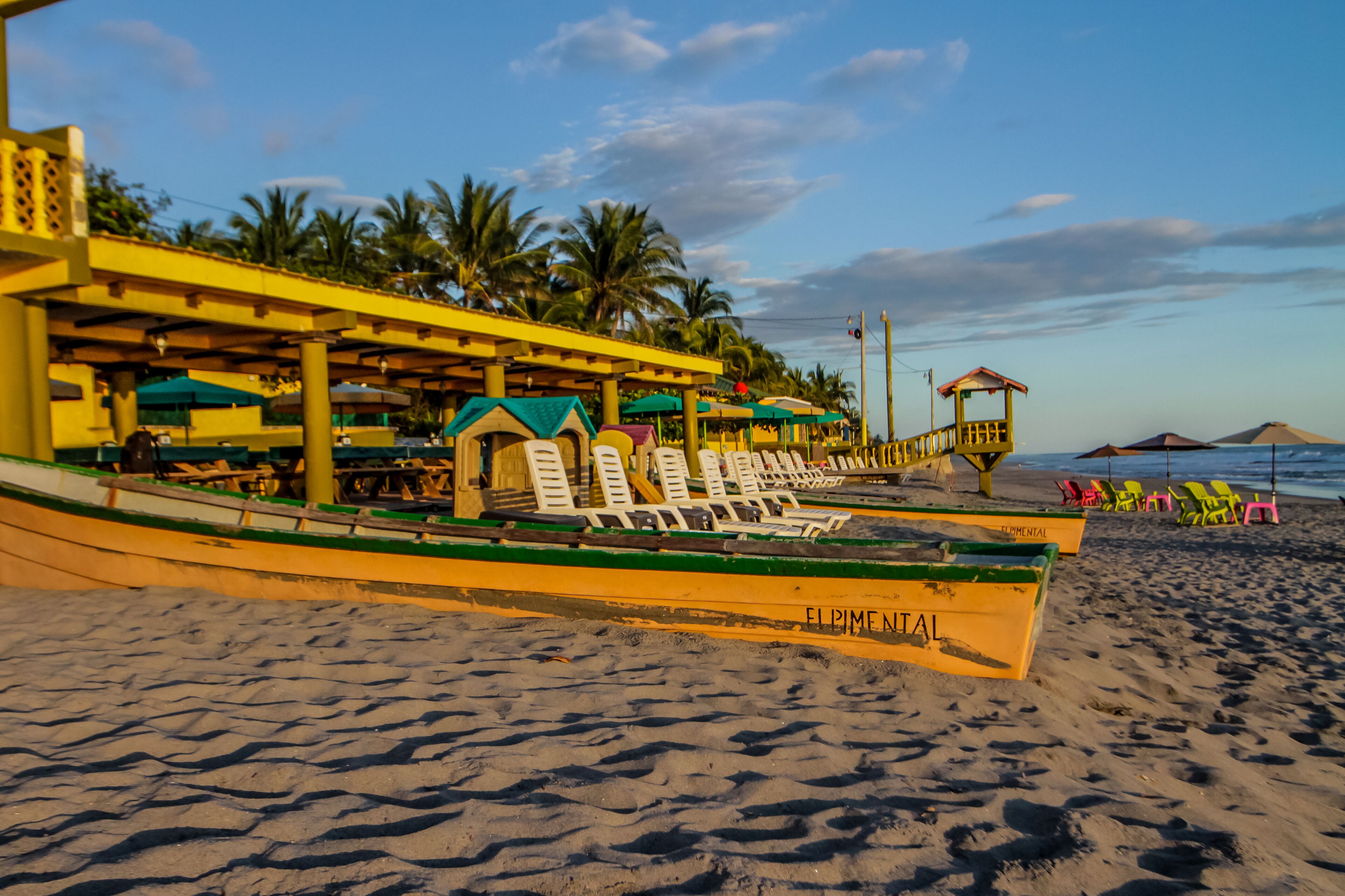 A beachside restaurant with outdoor seating and a boat moored nearby.