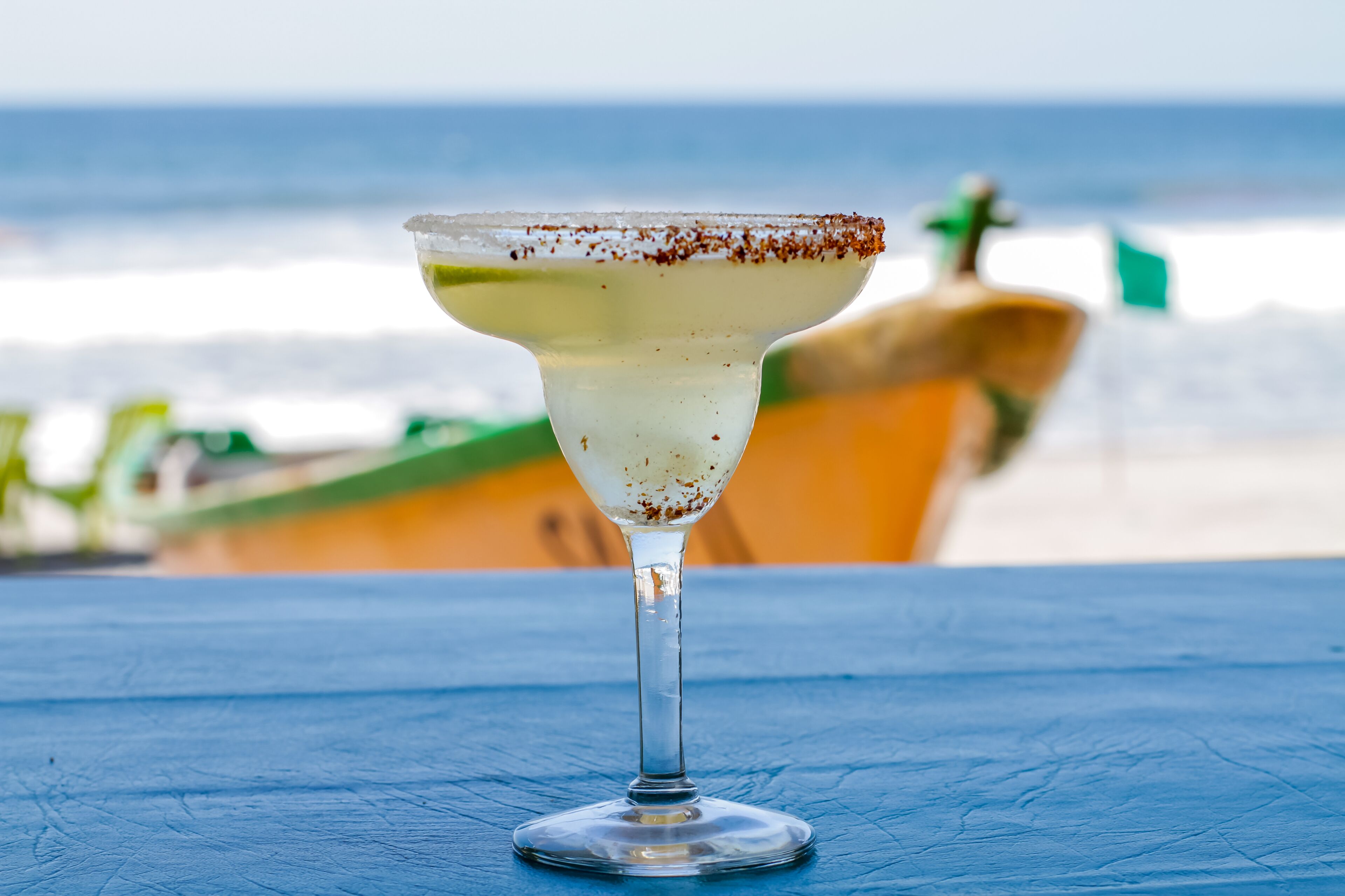 A margarita on a blue table with a beach and ocean in the background.