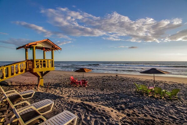 Una playa con una torre de salvavidas, sillas de descanso y sombrillas.