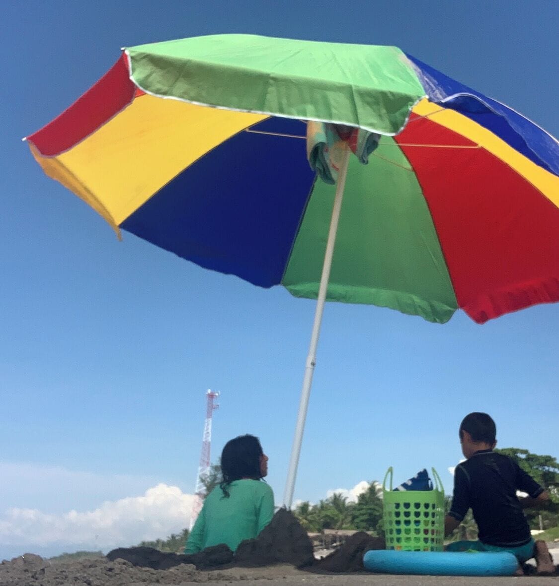 Dos personas sentadas bajo un colorido parasol de playa.