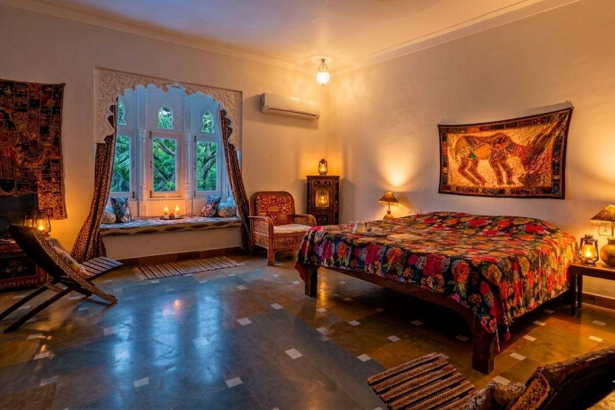 Une chambre avec un grand lit, une fenêtre ornée de volets décoratifs, une chaise et une tapisserie au mur.