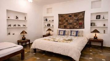 A bedroom with a large bed, two bedside tables, a nightstand, a ceiling fan, and a quilted wall hanging.