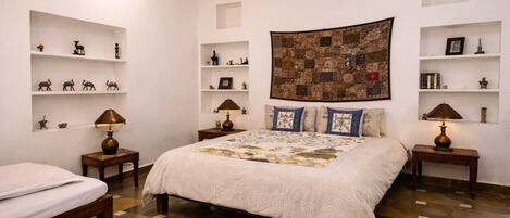 A bedroom with a large bed, two bedside tables, a nightstand, a ceiling fan, and a quilted wall hanging.