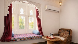 A room with a window seat, a wicker chair, and a small table with water bottles. - Hibiscus Heritage - A Lake View Hotel in Udaipur (Udaipur)