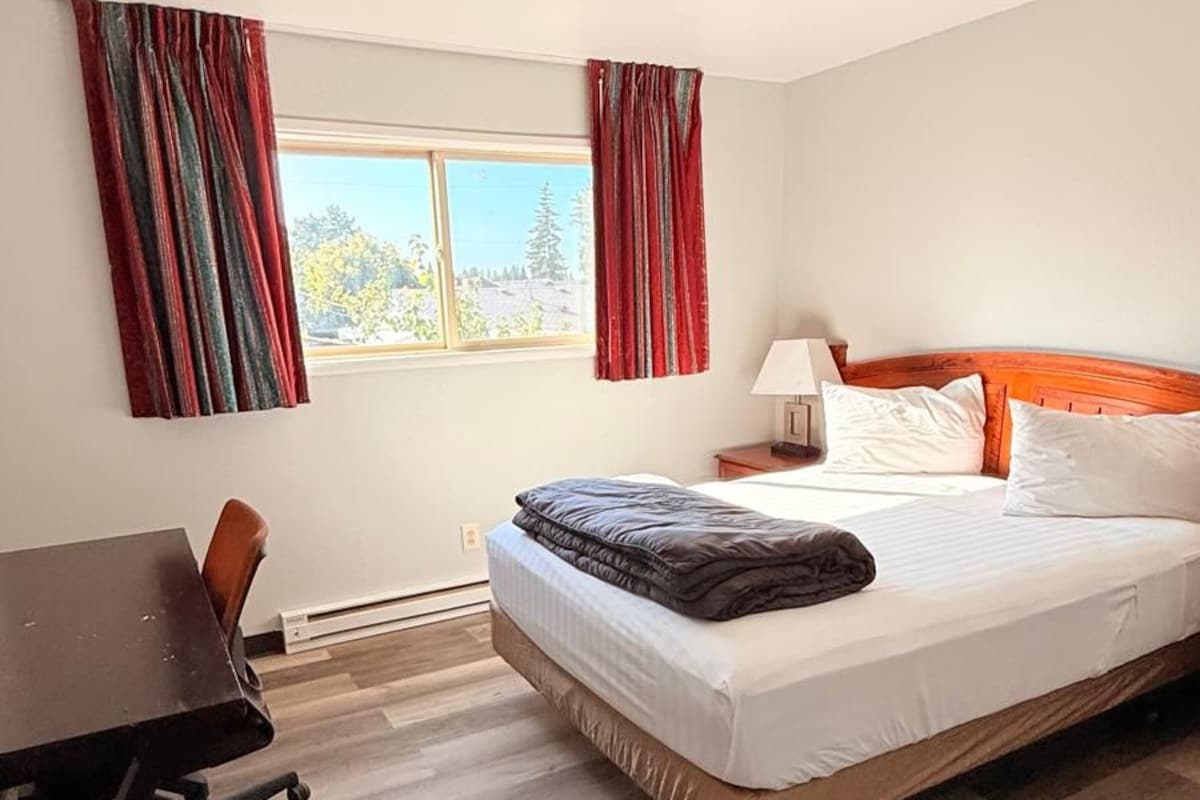 A hotel room with a bed, a desk, a chair, and a window with curtains.