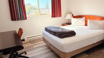 A hotel room with a bed, a desk, a chair, and a window with curtains.