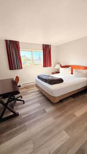 A hotel room with a bed, a desk, a chair, and a window with curtains. - Portland Value Inn & Suites Near PDX Airport (Portland)