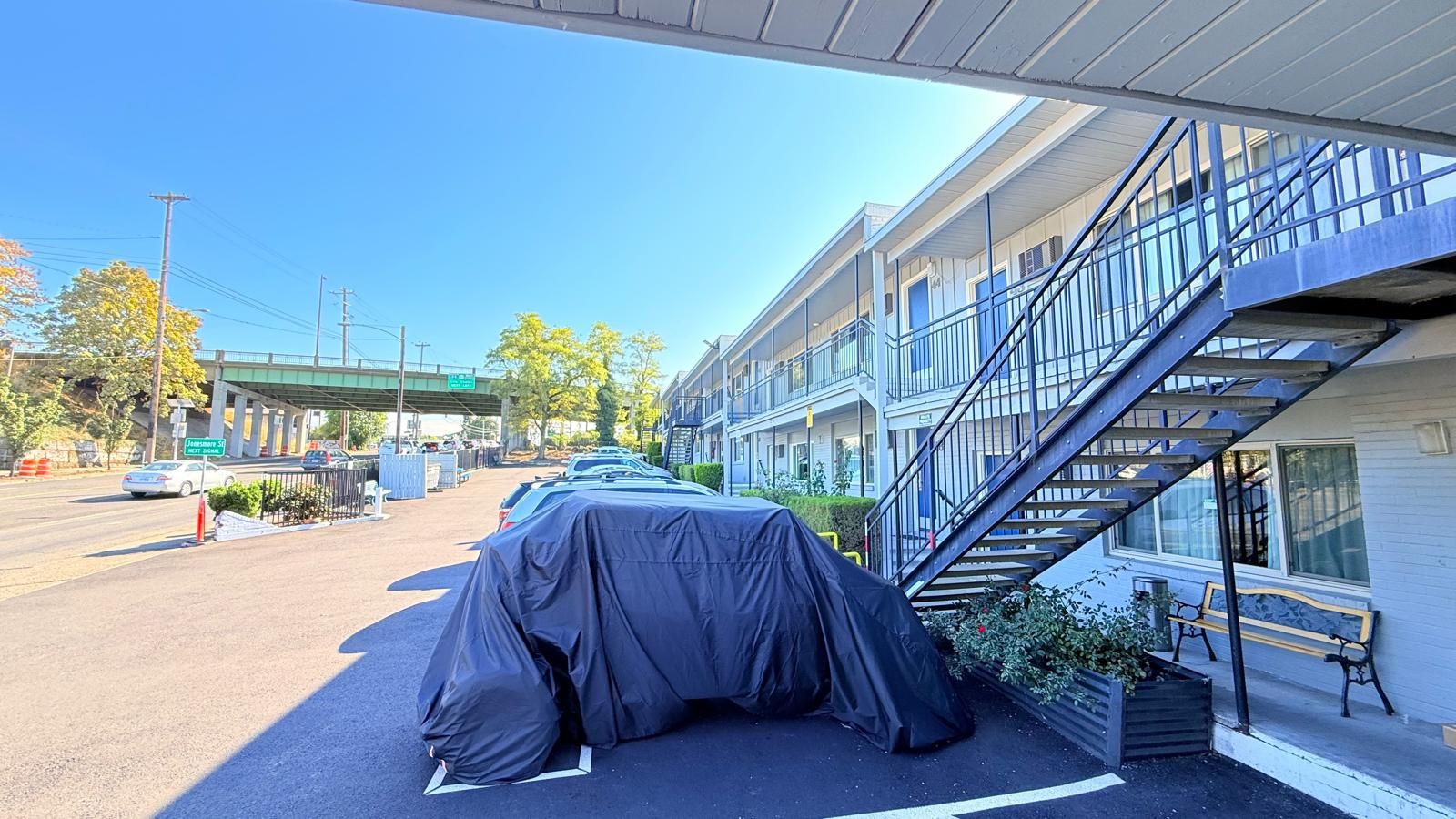 A covered car parked in front of a building with a staircase leading to an upper level.
