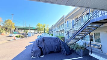 A covered car parked in front of a building with a staircase leading to an upper level.