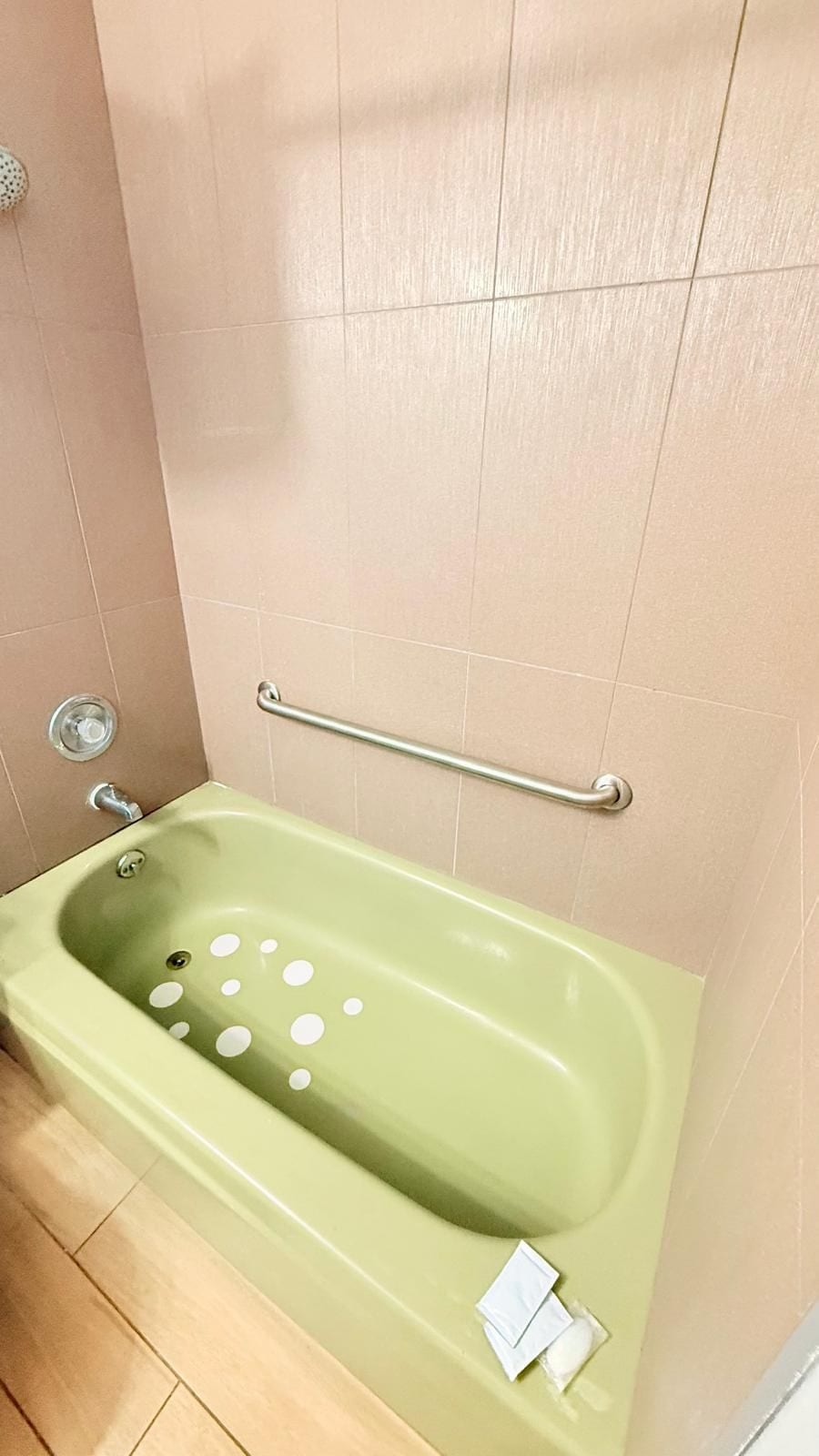 A green bathtub with a grab bar, a showerhead, and a small white object on the floor.