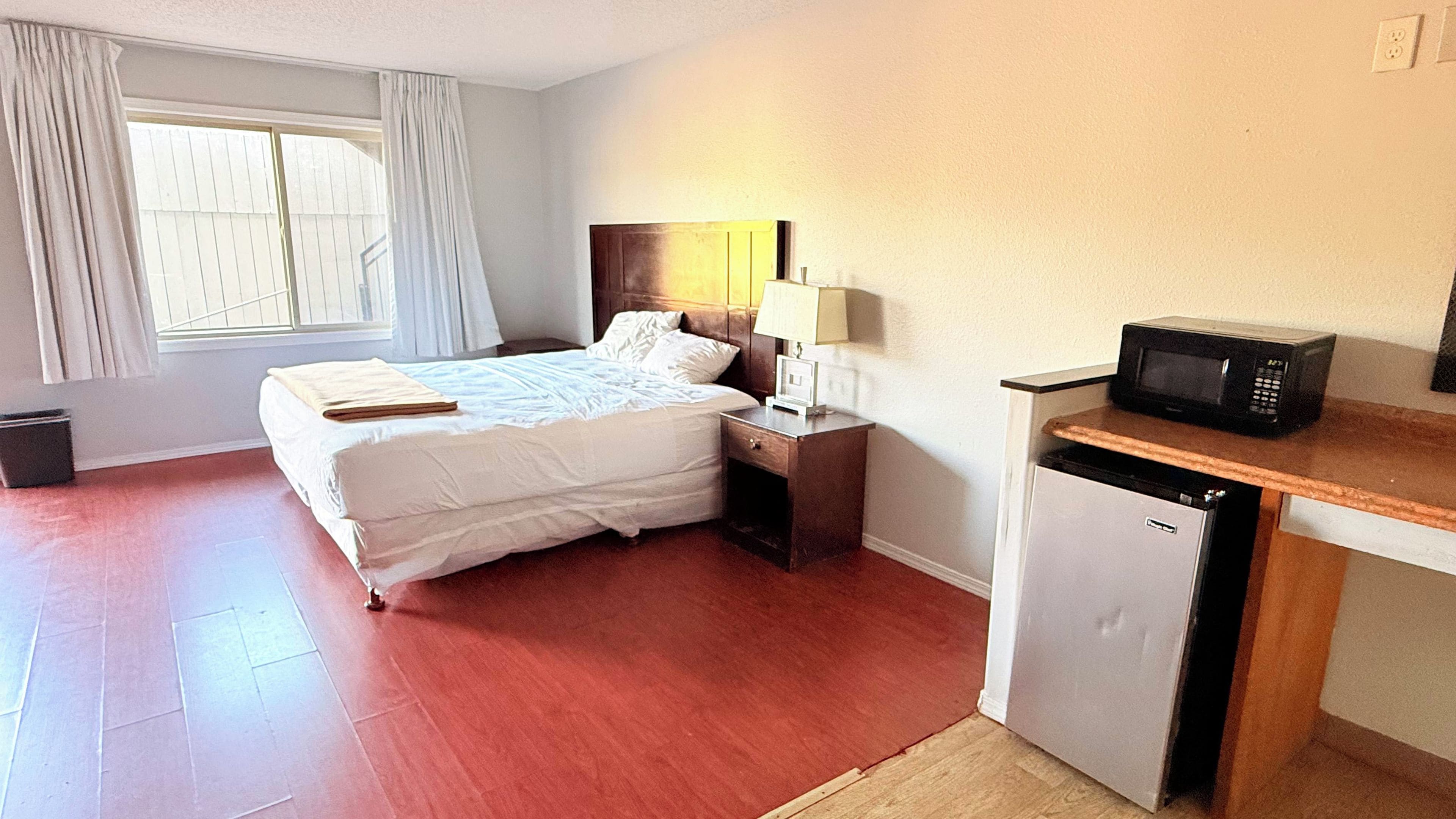 A hotel room with a bed, bedside table, lamp, and a microwave.