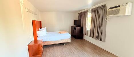 A hotel room with a bed, a wooden nightstand, a television, and a window with curtains.