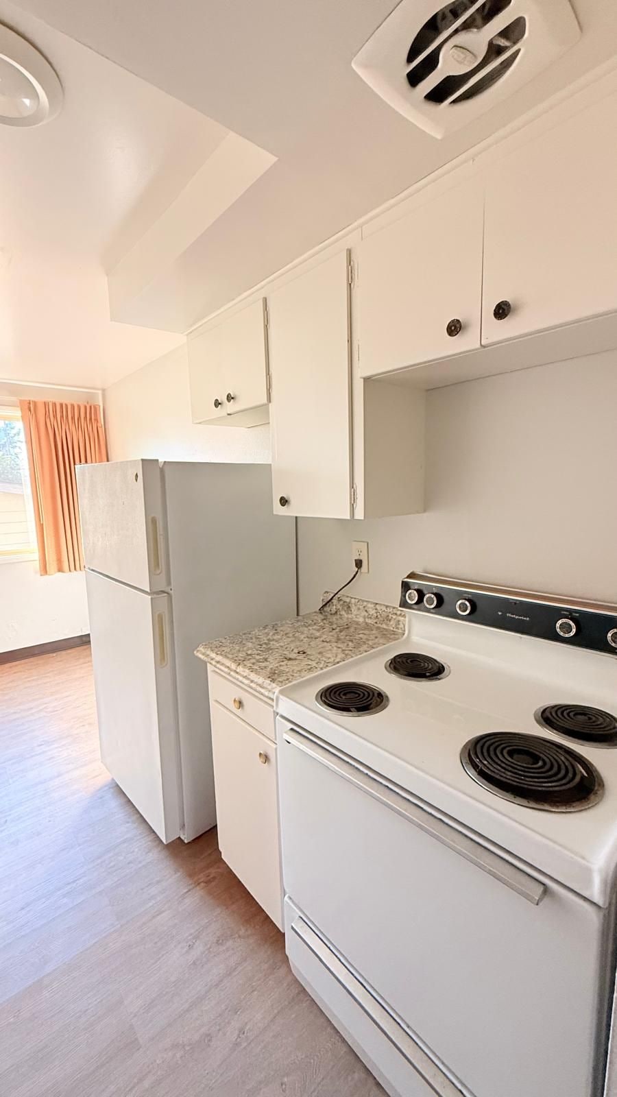 A kitchen with white cabinets, a white refrigerator, a stove with four burners, and a vent on the ceiling.