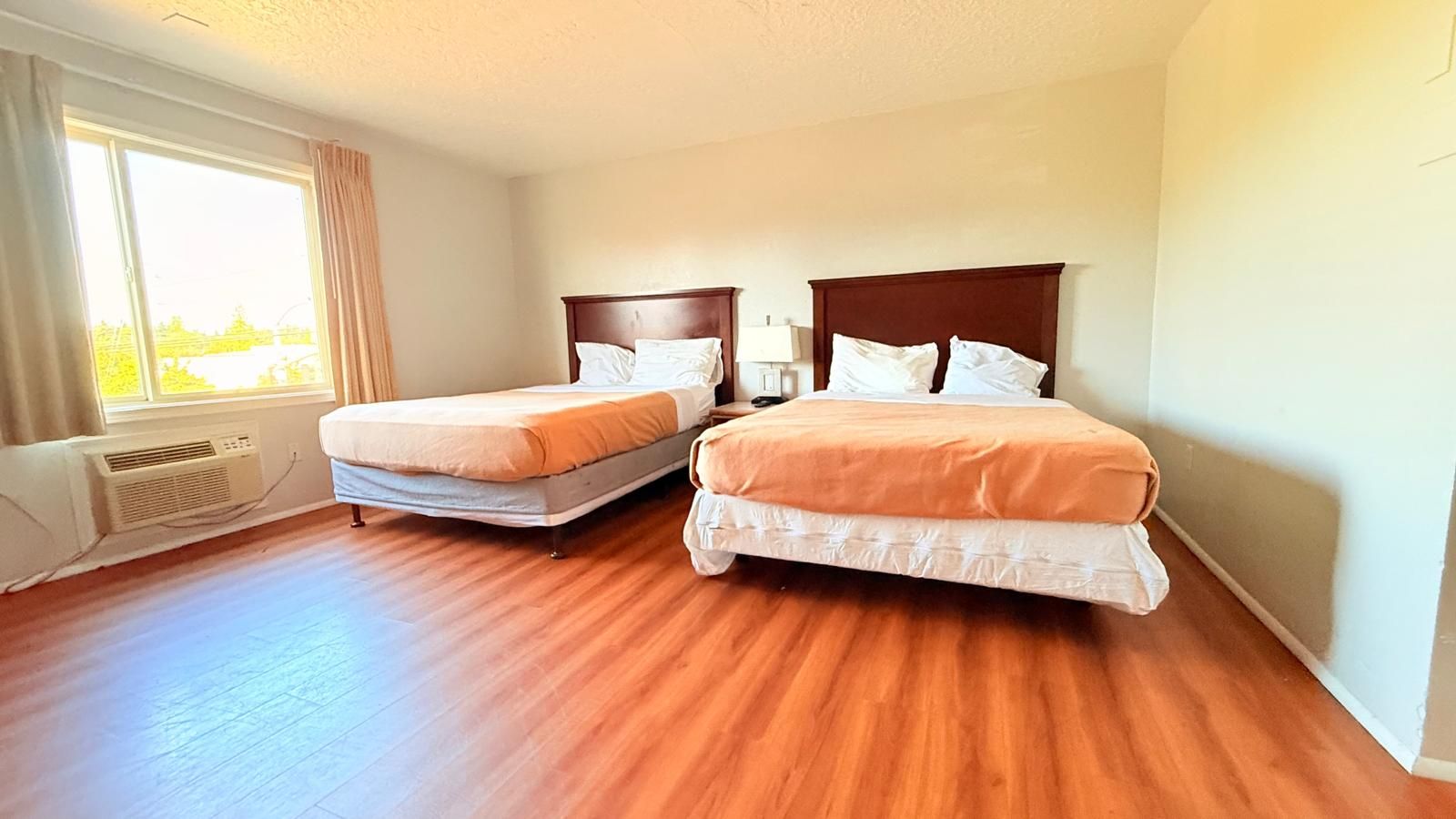 Habitación de hotel con dos camas, un ventanal grande y aire acondicionado integrado.