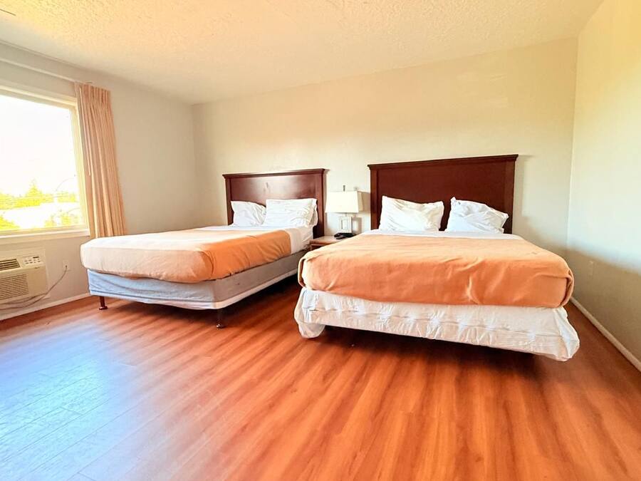 A hotel room with two beds, a large window, and a built-in air conditioning unit.