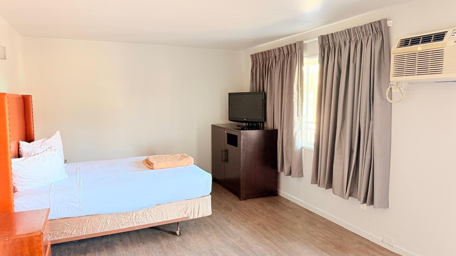 Een hotelkamer met een bed, een televisie op een kast en gordijnen voor het raam.